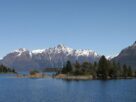 Mesa com câmera, caderno e xícara diante de uma janela com vista para lago e montanhas, em imagem ilustrativa de Bariloche.