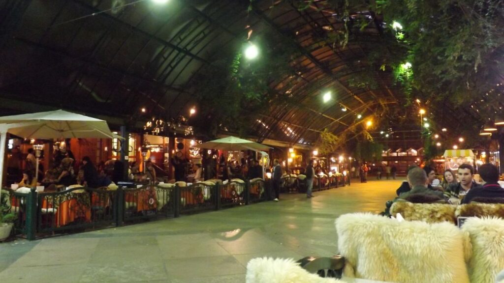 Rua Coberta em Gramado à noite, com restaurantes e mesas sob a cobertura.
